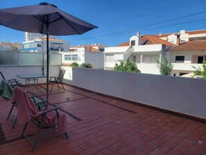 A rooftop terrace with a table, chairs, and an umbrella.