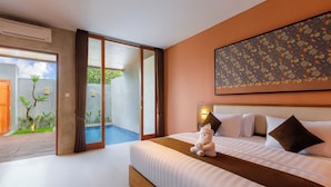 Habitación de hotel con una cama, una pequeña estatua, un cuadro y una puerta corredera que da a un balcón con plantas.