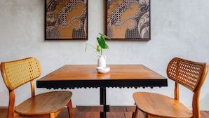 Una mesa de madera con borde negro, dos sillas de madera con respaldo trenzado y un jarrón blanco con una planta sobre la mesa.