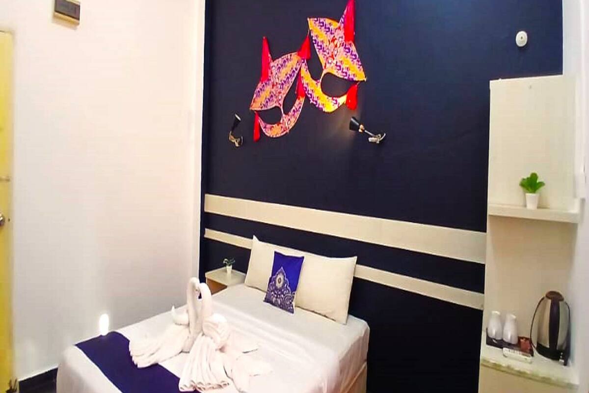 A hotel room with a bed, a wall-mounted artwork, a small shelf with toiletries, and a potted plant.