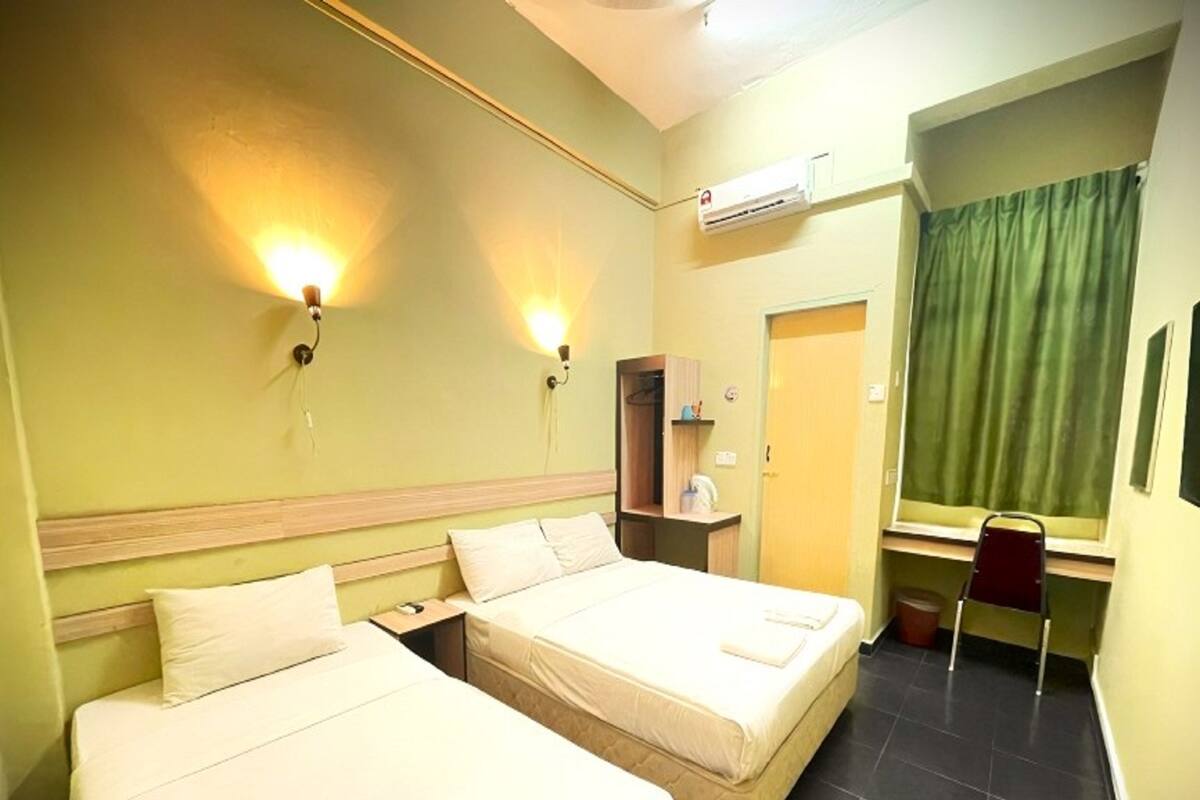 A hotel room with two beds, a desk, a chair, an air conditioning unit, and a green curtain.