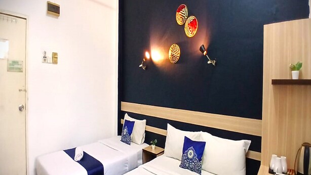 Habitación de hotel con dos camas, una pared oscura con luces decorativas, un estante de madera con una planta y una cafetera.