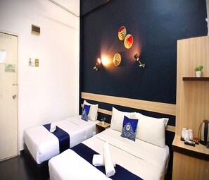 A hotel room with two beds, a dark wall with decorative wall lights, a wooden shelf with a plant, and a coffee machine. - Alia Express Green Mango, Kota Bharu (Kota Bharu)