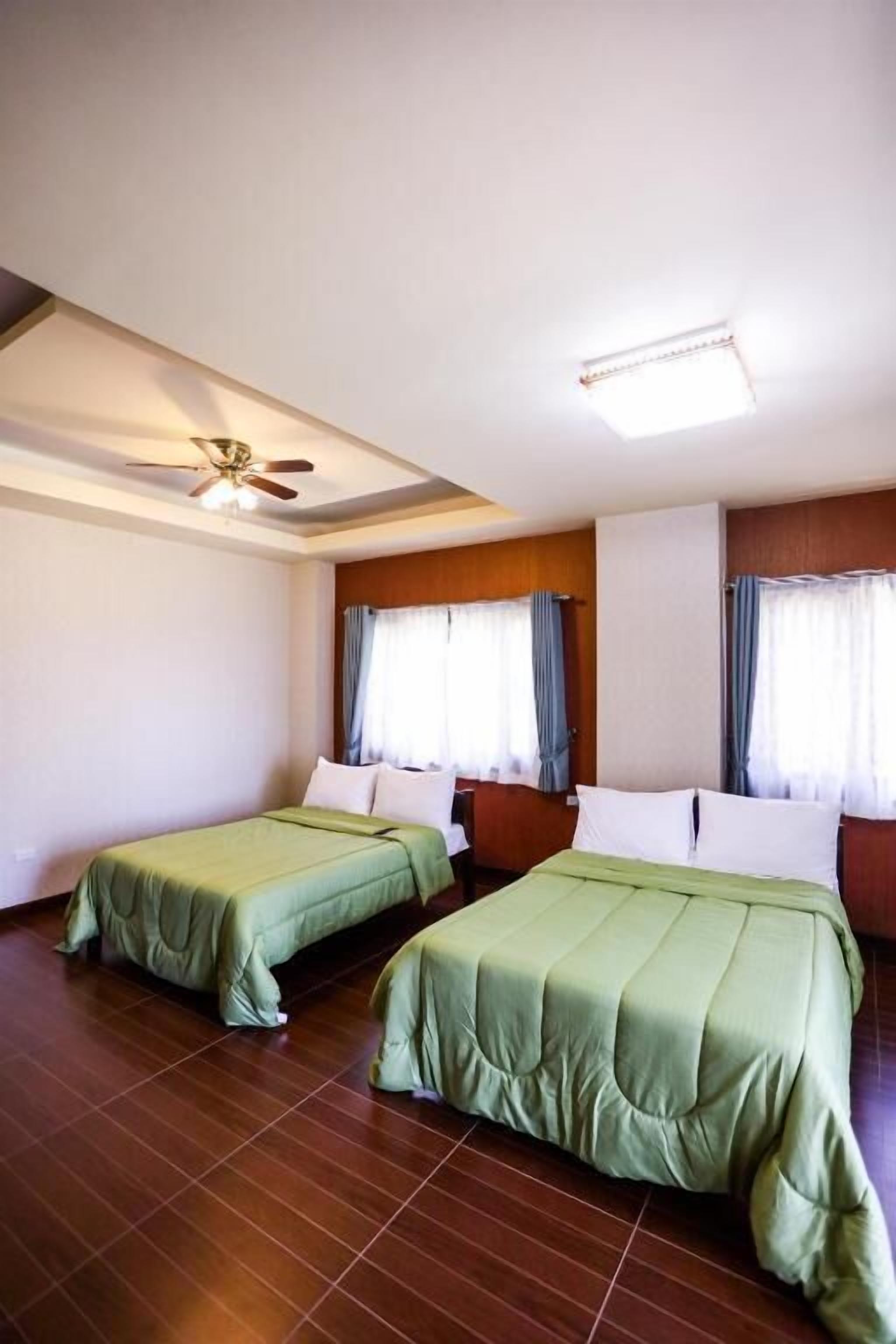 Une chambre d’hôtel avec deux lits simples, un ventilateur de plafond et une grande fenêtre avec des rideaux.