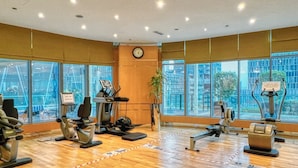Un gimnasio con equipo de ejercicio, ventanas amplias y un reloj en la pared.