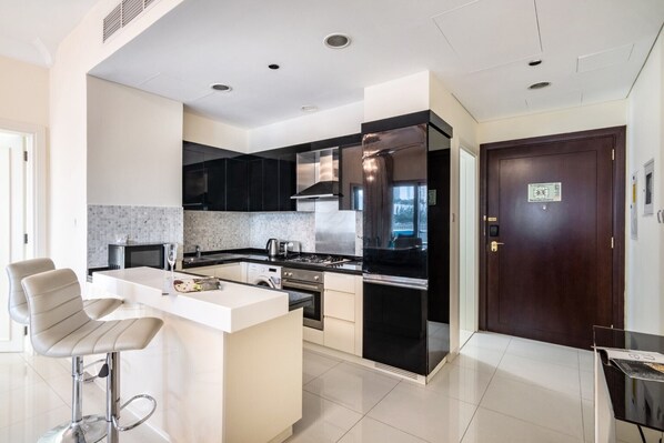 A modern kitchen with a central island, stainless steel appliances, and a dark wooden door. - Amazing 1 BR Apartment Damac Mall Street (Dubai)