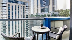 Un balcón con sillas de mimbre y una mesa, con vistas a un paisaje urbano con edificios altos.