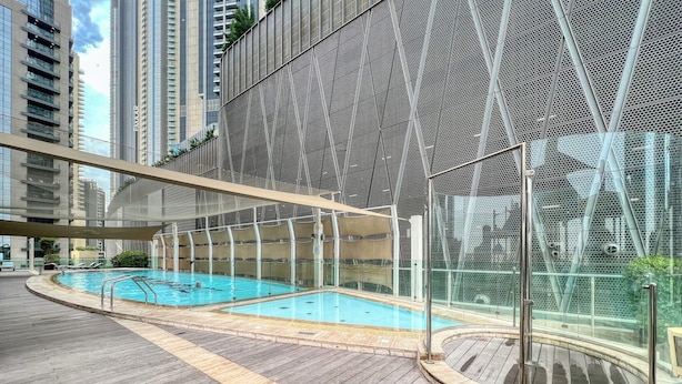 Una piscina moderna al aire libre con cubierta de madera, rodeada de edificios altos.