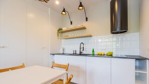 Een moderne keuken met witte kasten, een zwart aanrecht en een rvs afzuigkap. Er is een eettafel met stoelen en een hangplant.