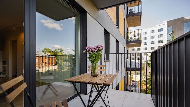 Een balkon met een houten tafel en een bloevas, met uitzicht op een stadsbeeld.