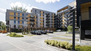 Een meerlaags woongebouw met balkons, een parkeerplaats en een aangelegde tuin.