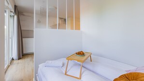 Een slaapkamer met een bed, een houten nachtkastje met een bord eten, witte muren en een raam met gordijnen.