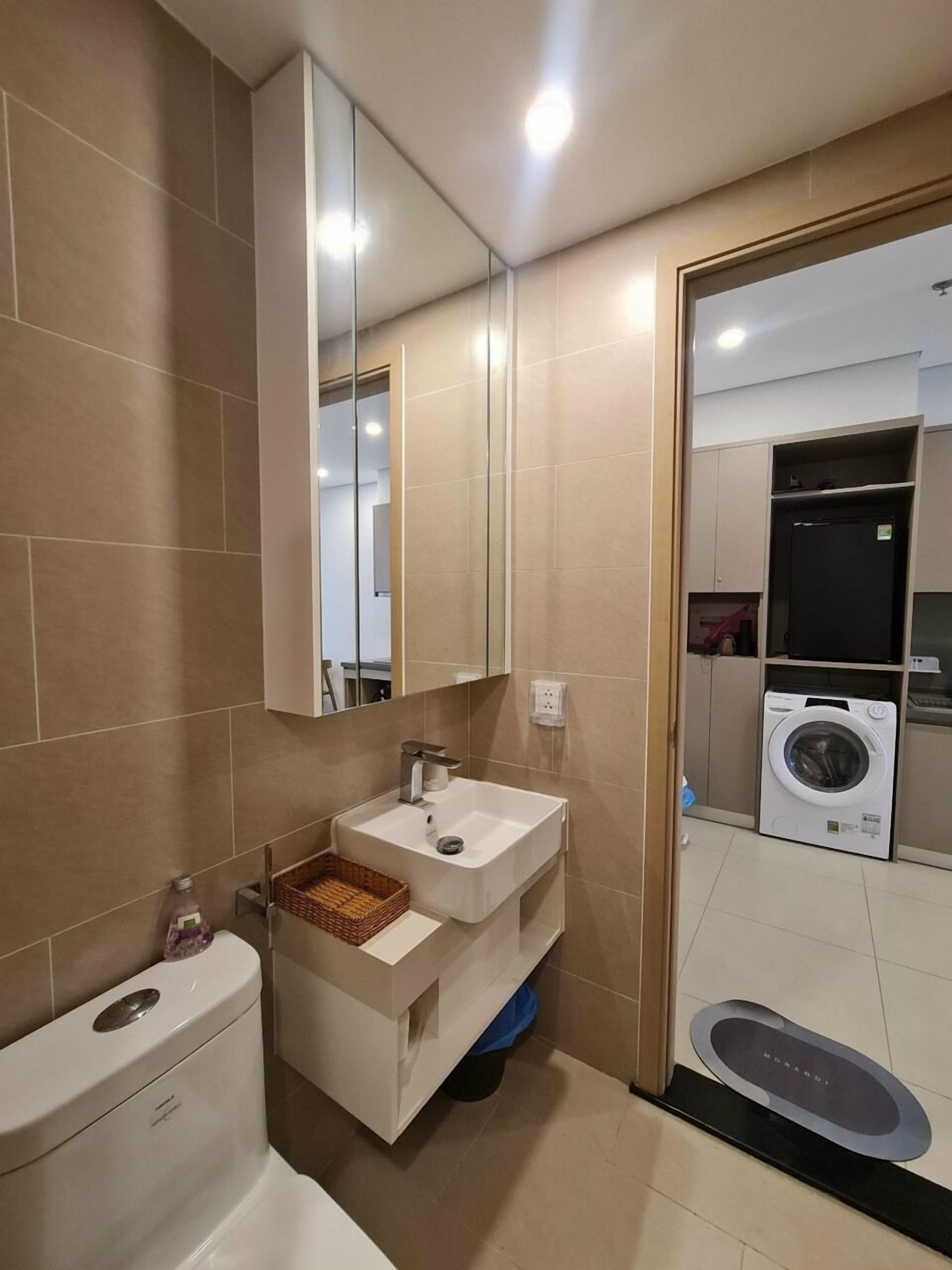 A modern bathroom with a double sink, a toilet, a mirror, and a washing machine.