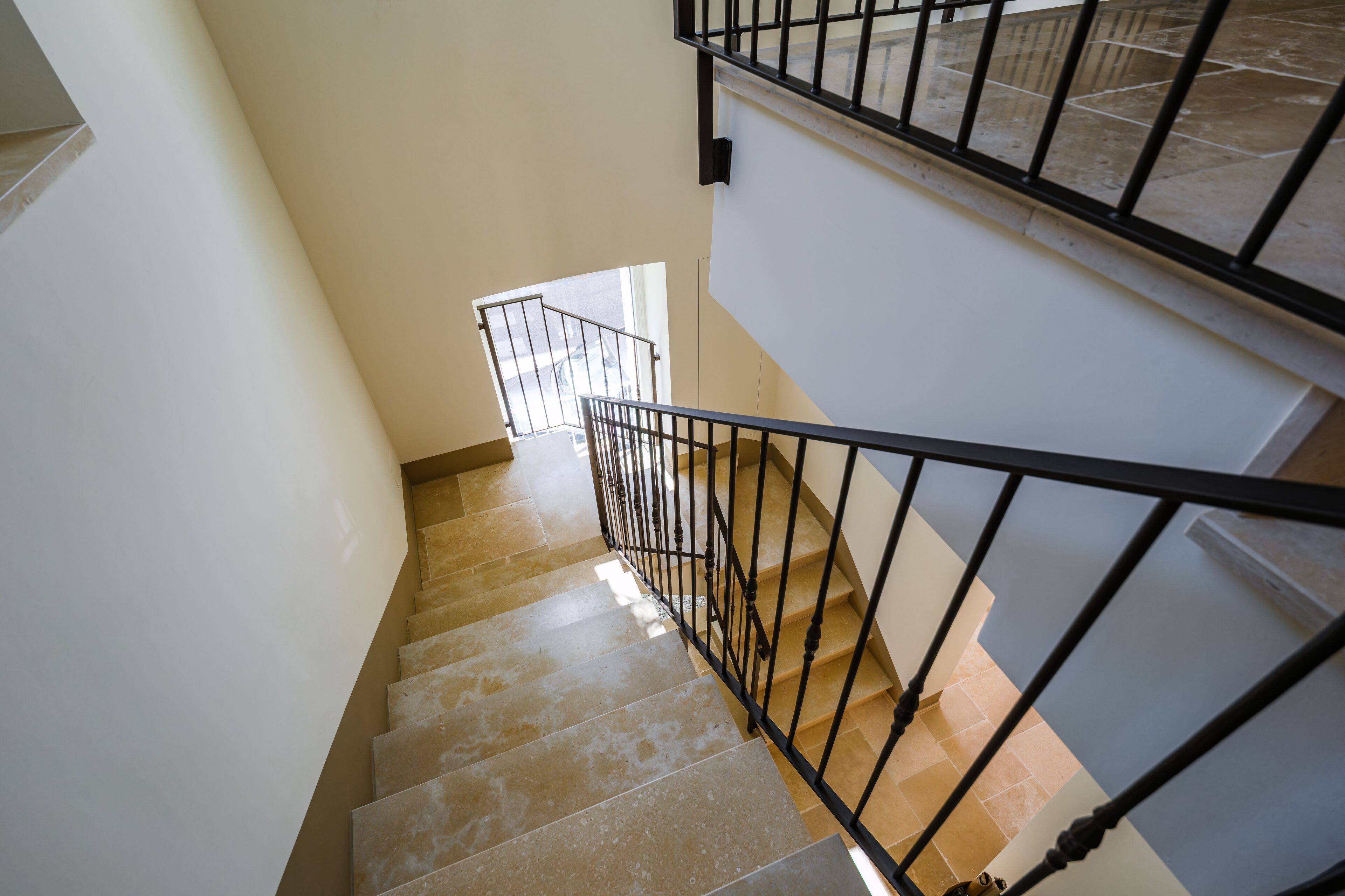 Un escalier avec une rampe en métal, des murs de couleur beige et une fenêtre en haut.