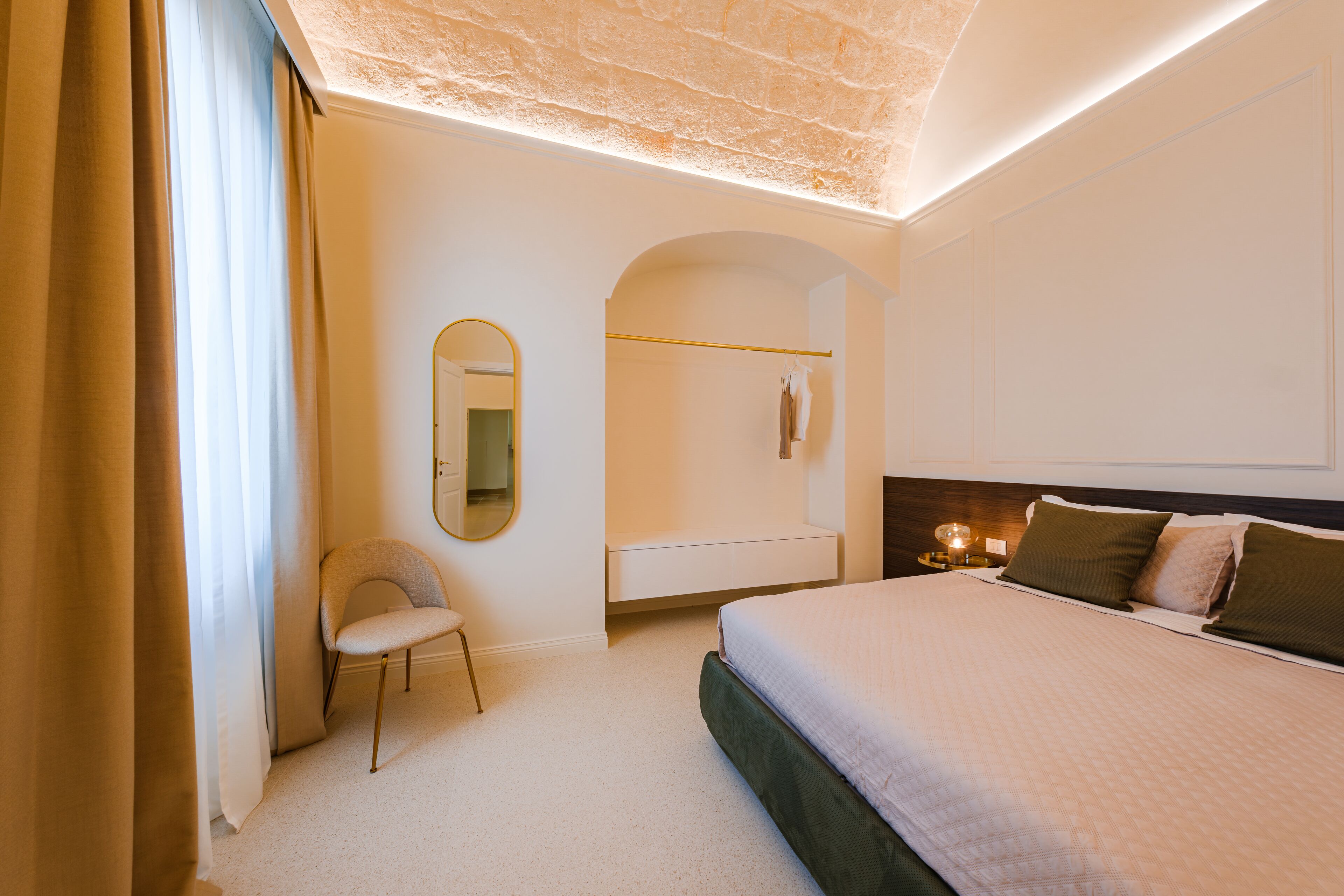 A modern bedroom with a large bed, a bedside table with a lamp, a chair, a mirror, and a wardrobe.