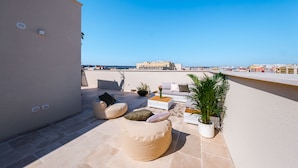 A rooftop terrace with a beige wall, a white sofa, a beige bean bag, a coffee table, and a potted plant. - Palazzo Clemente (Monopoli)