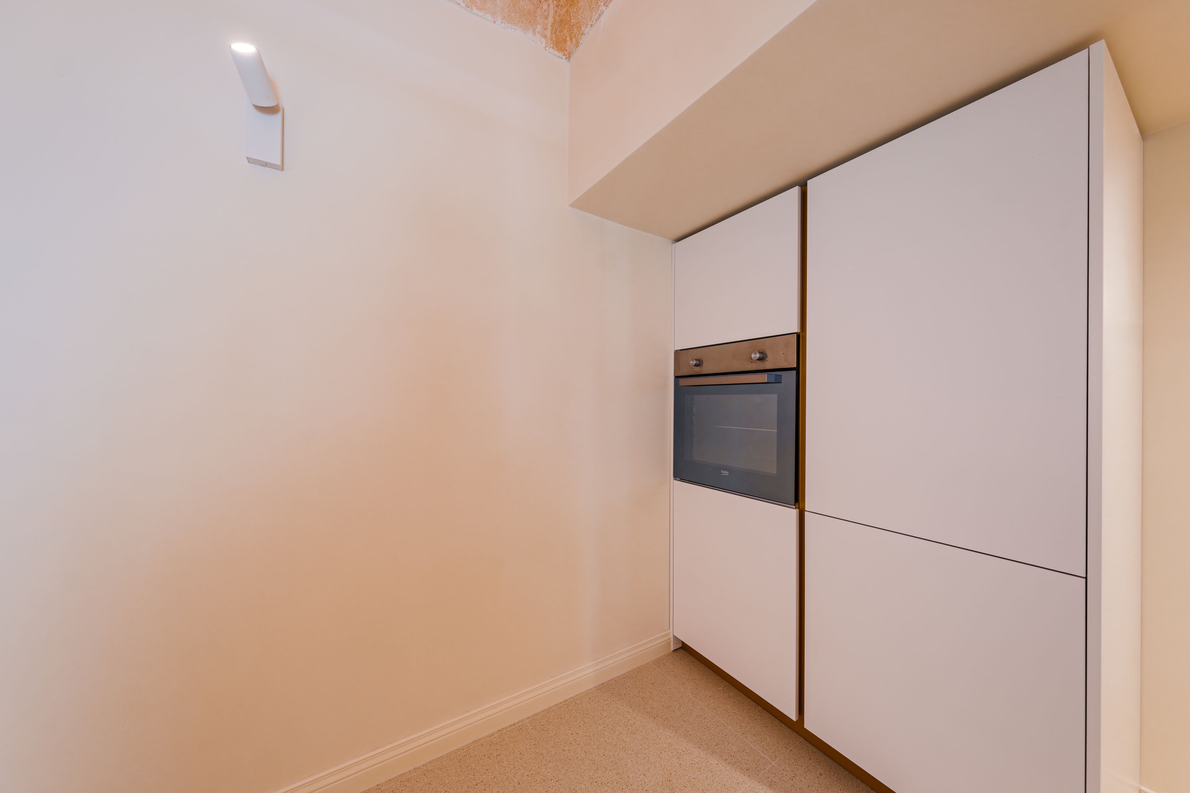 A compact kitchen with built-in appliances, a light fixture, and a tiled floor.