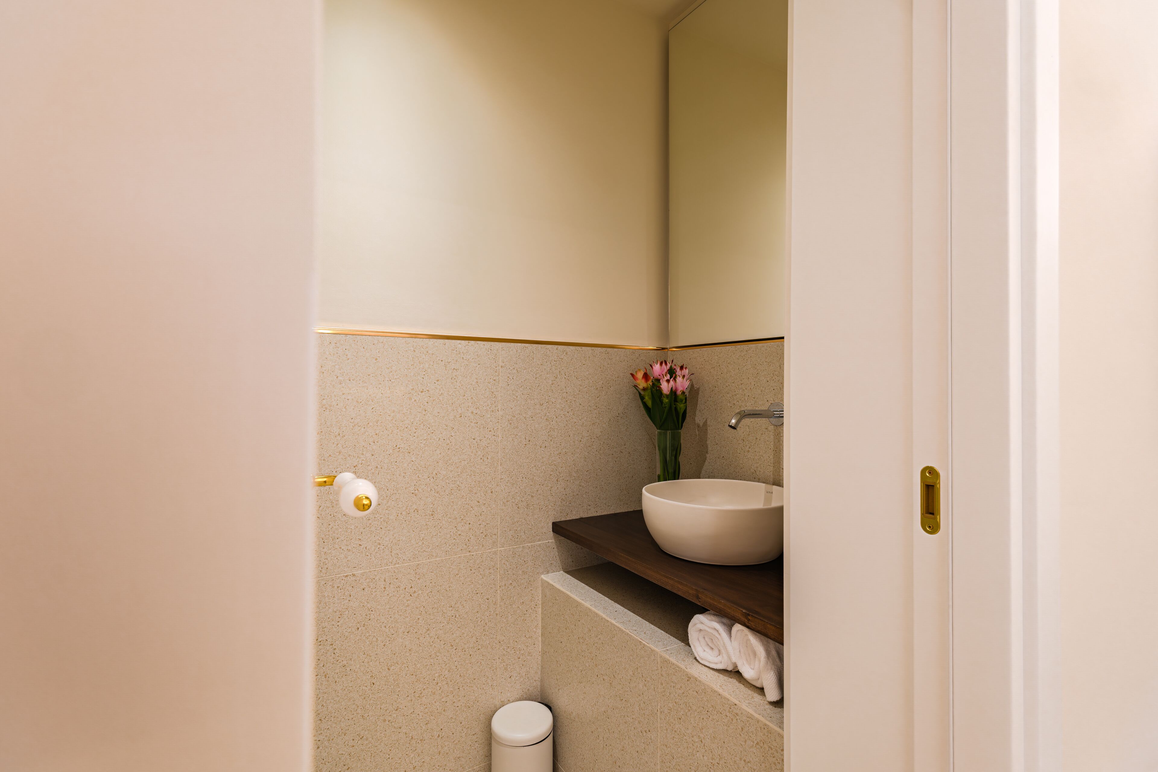 A bathroom with a white sink, a mirror, and a vase with flowers.