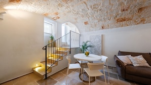 A spacious living area with a staircase, a round dining table, and a brown sofa. - Palazzo Clemente (Monopoli)