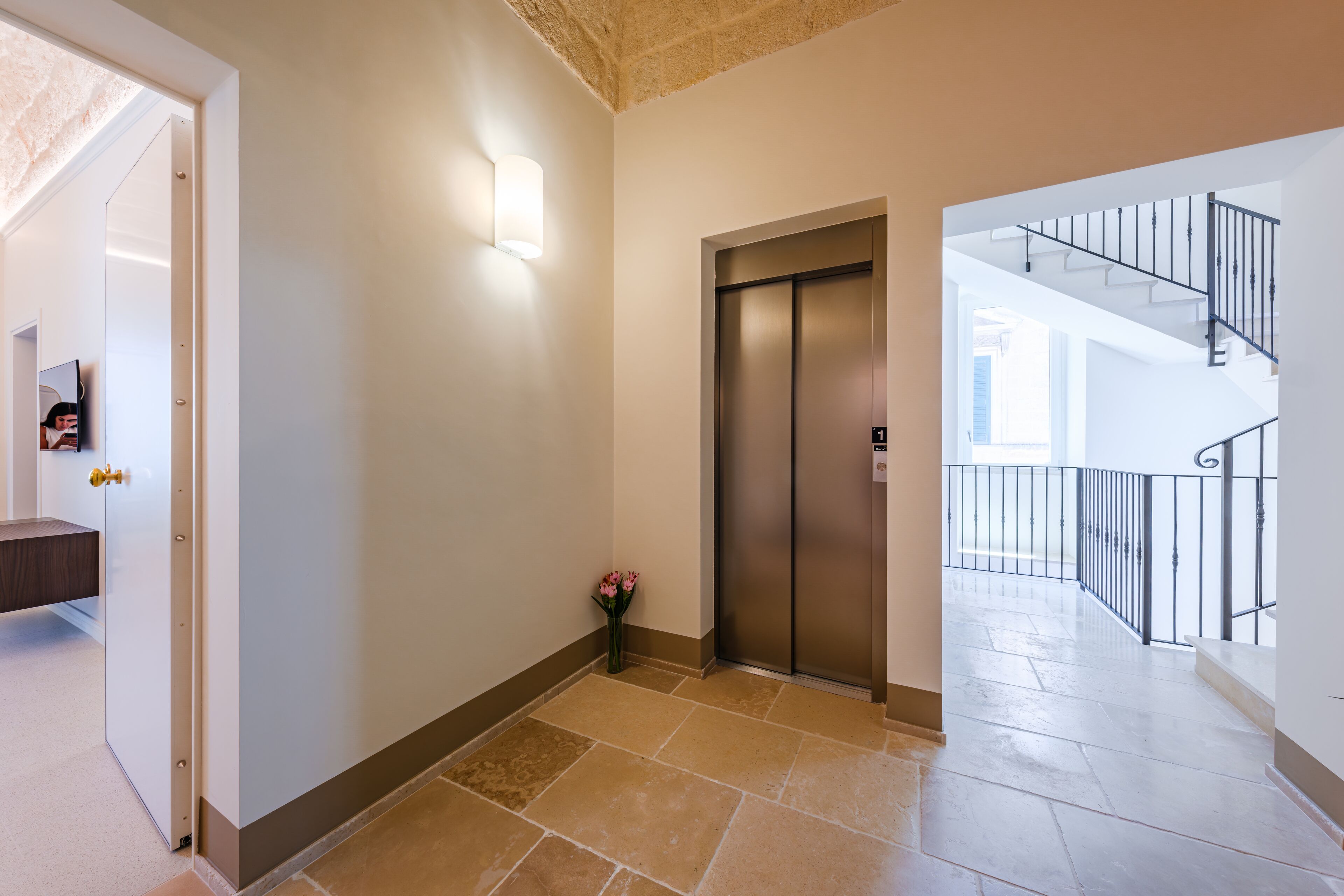 A hallway with a tiled floor, a wall-mounted light, an elevator, and a staircase.