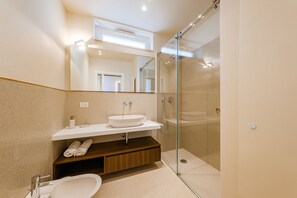 Un baño moderno con ducha de vidrio, un lavabo blanco y un mueble de tocador de madera.