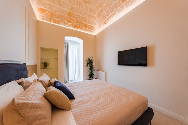 A bedroom with a large bed, a flat-screen TV mounted on the wall, and a small plant on a shelf.