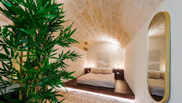 A modern bedroom with a stone ceiling, a large bed, bedside lamps, and a mirror. - Palazzo Clemente (Monopoli)