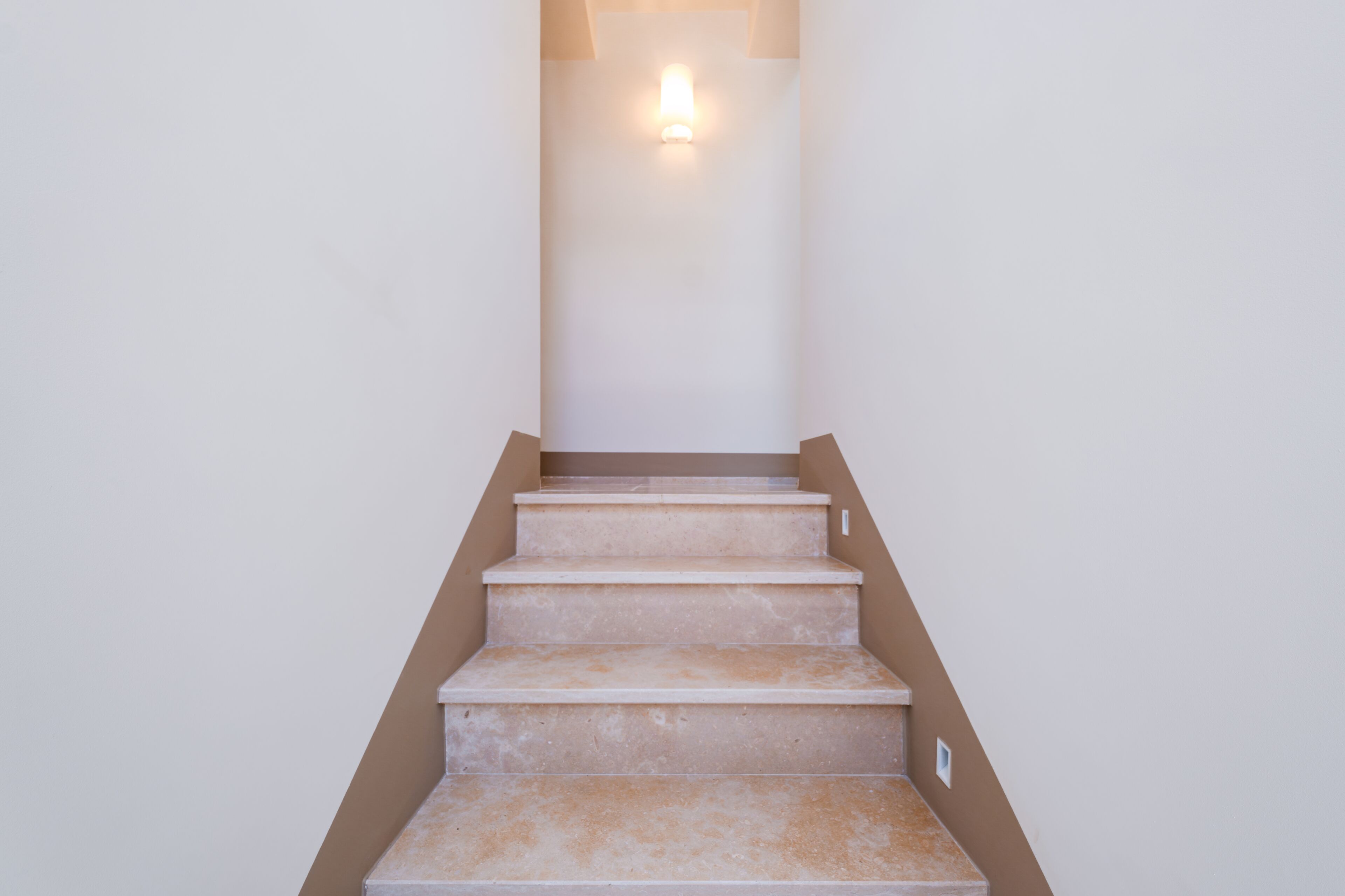 A set of beige carpeted stairs leading up to a landing with a wall-mounted light fixture.