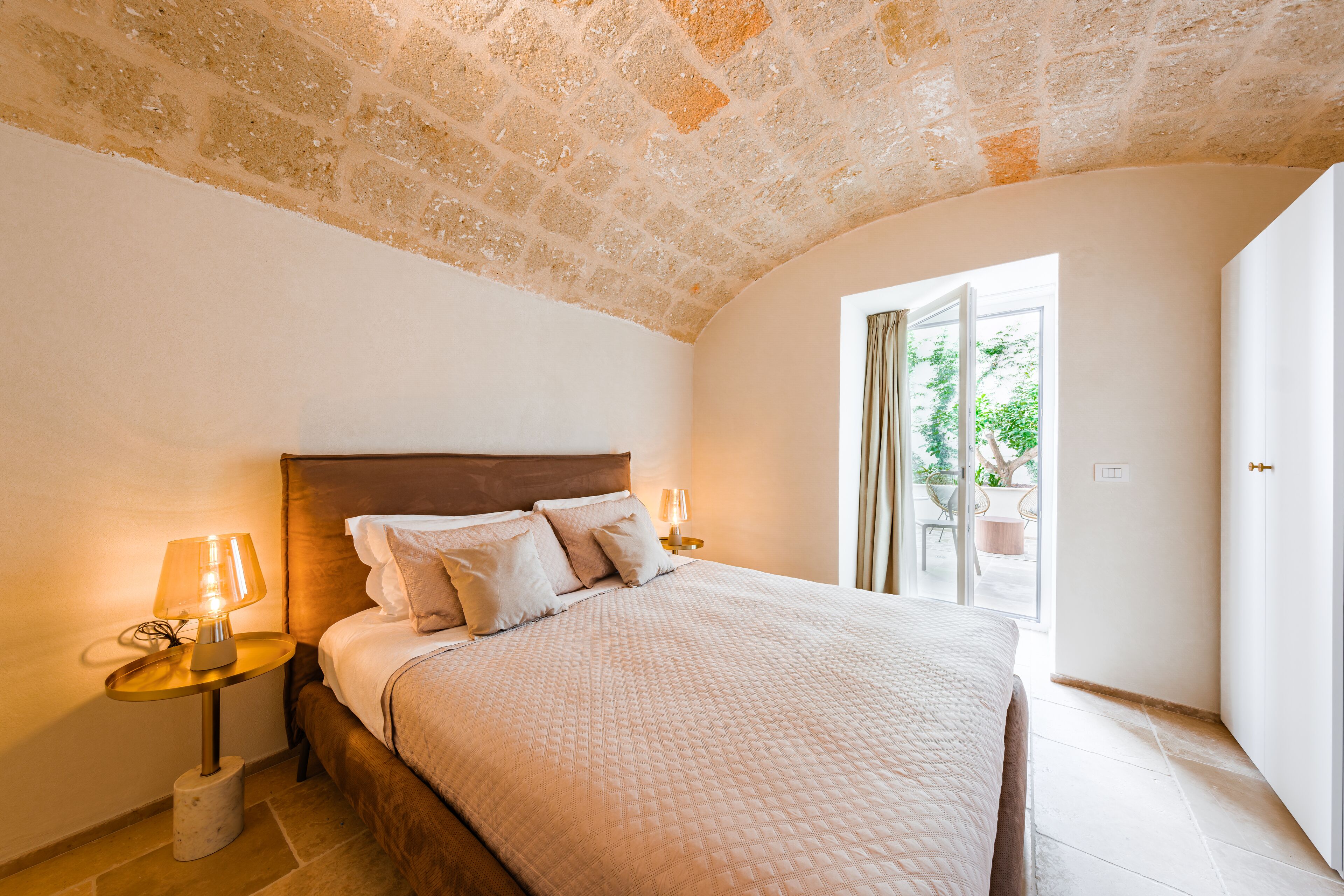 A bedroom with a large bed, two bedside tables with lamps, a wooden headboard, and a view of the outdoors through a sliding glass door.