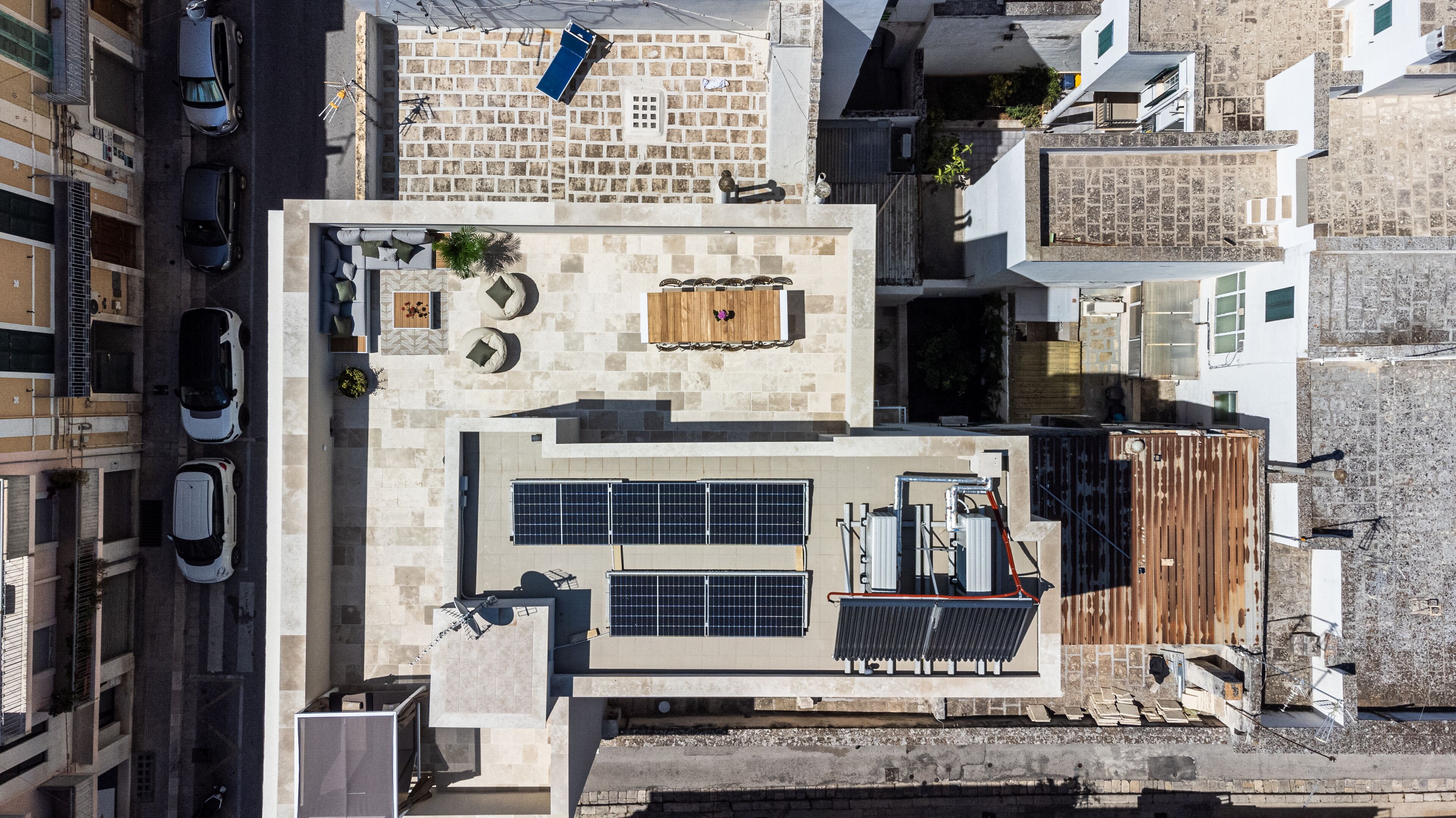 An aerial view of a residential building with a rooftop terrace featuring solar panels, outdoor seating, and a small table.