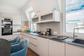 A modern kitchen with built-in appliances, a window with a view, and a dining area with blue chairs.
