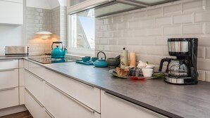 Una cocina moderna con armarios blancos, un ventanal sobre la encimera y diversos electrodomésticos.