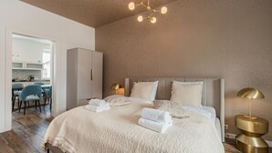 Un dormitorio con una cama grande, una lámpara de noche y vista a la cocina.