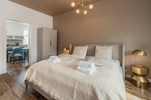 Ein Schlafzimmer mit einem großen Bett, einer Nachttischlampe und Blick in die Küche.