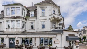 Un edificio histórico con numerosas ventanas y un balcón, que cuenta con mesas al aire libre y un letrero de restaurante.