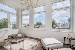 A room with large windows, a bed, a table, and a chandelier.