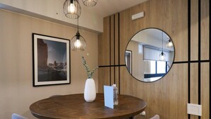 A round wooden dining table with chairs, a framed picture, a vase with greenery, a mirror, and pendant lights.