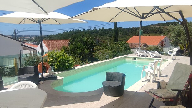 A rooftop pool area with lounge chairs, umbrellas, and a view of the surrounding landscape.