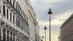 Una plaza pública con edificios históricos, una estatua y gente caminando.