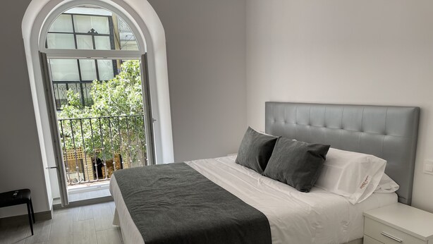 Un dormitorio con cama, una mesita de noche y ventana con vista a la vegetación.