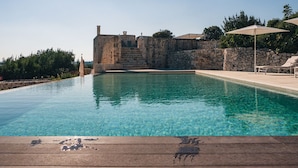 A clear swimming pool with a wooden deck in the foreground, stone walls, and a stone building in the background. - Masseria Minetta (Cisternino)