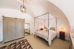 A bedroom with a four-poster bed, a wardrobe, a bedside table with a lamp, and a mirror. - Masseria Minetta (Cisternino)