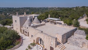 A stone building with a flat roof, multiple chimneys, and a covered outdoor seating area. - Masseria Minetta (Cisternino)