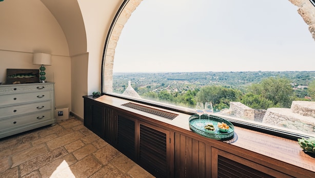 A room with a large arched window overlooking a scenic landscape. - Masseria Minetta (Cisternino)