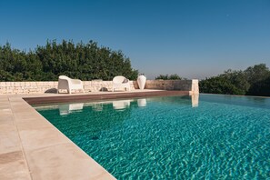 A clear blue pool with white lounge chairs and a stone wall. - Masseria Minetta (Cisternino)