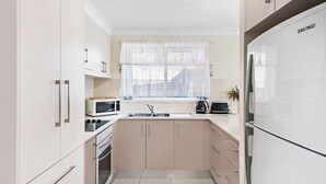 A modern kitchen with white cabinets, a microwave, a stove, a sink, and a refrigerator.