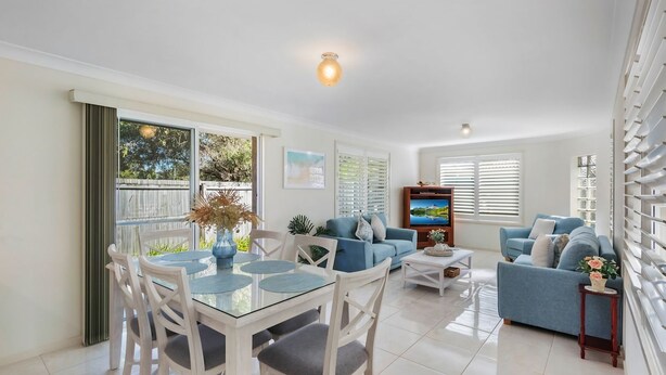 A modern living room with a glass dining table, blue sofas, and a TV.