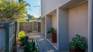 A narrow pathway leading to a building with a wooden fence on one side and potted plants on the other.