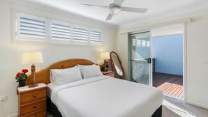A bedroom with a bed, a nightstand with a lamp, a mirror, and a view of a balcony.
