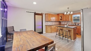 Una cocina moderna con armarios de madera, una isla central con taburetes y un puertas correderas de vidrio que dan a un comedor con mesa y sillas de madera.